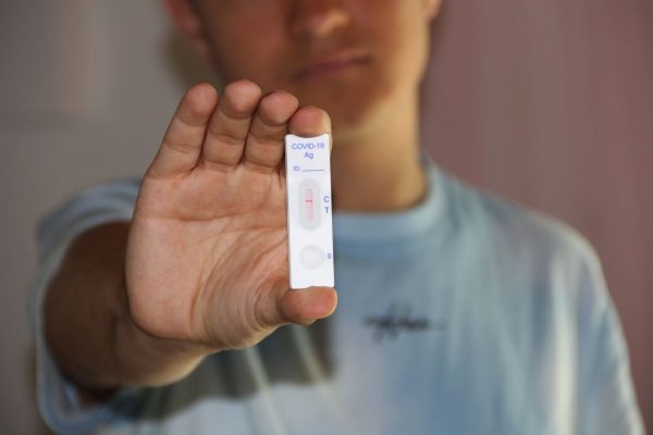 Close-up of a man holding a COVID-19 antigen test kit indoors.
