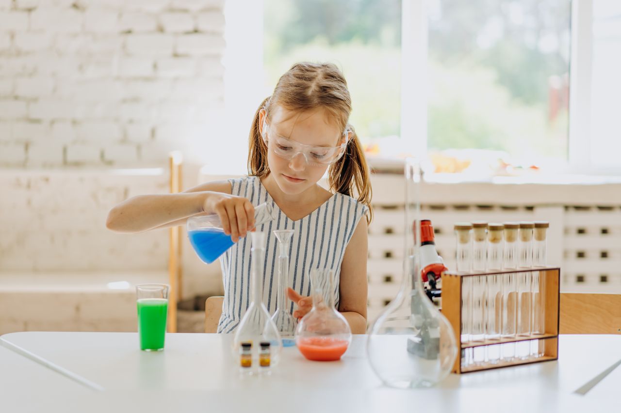 A girl conducting a science experiment with flasks in a bright classroom setting.