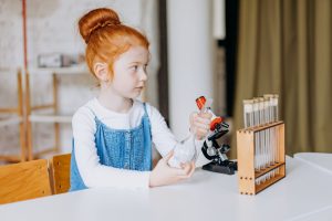 A young girl explores science with test tubes and microscopes in a bright indoor setting.